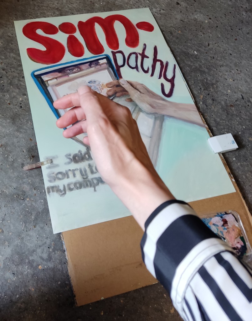 A close-up of an artist's hand holding a paintbrush above a partially completed canvas featuring the word 'SIM-pathy' in bold red letters, depicting two hands and eyes, with handwritten notes below.